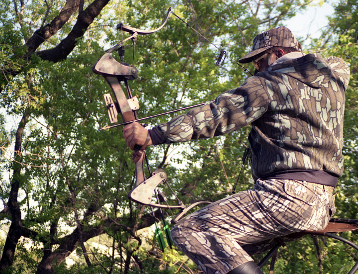 Doc taking aim with his bow while practicing in his back yard. He is elevated in a tree stand.